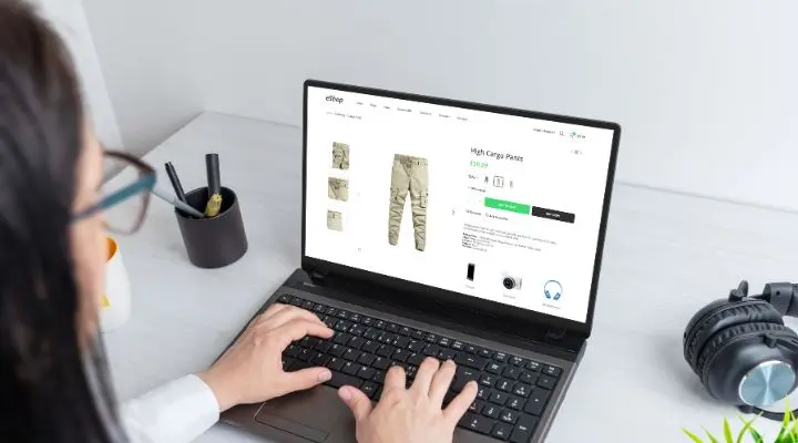 Persona buscando pantalones cargo altos en una computadora portátil, con auriculares y una taza de bolígrafos adornando el escritorio, creando un ambiente perfecto para interactuar con Contenido Evergreen.