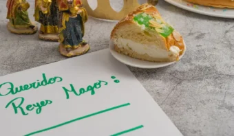 Una nota con la leyenda "Queridos Reyes Magos" junto a una rebanada de pastel en un plato, tres figuras y una corona dorada.