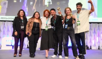 Un grupo de seis personas, radiantes de orgullo y sosteniendo sus trofeos en el escenario de un evento, donde también tuvieron el honor de instalar nuestro logotipo.