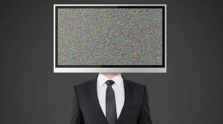 Una persona con traje y un televisor que muestra estática sobre su cabeza, que recuerda a la publicidad subliminal, se encuentra de pie sobre un fondo gris.