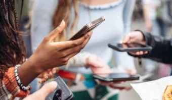 Varias personas sosteniendo teléfonos inteligentes, enfocándose en las pantallas, con un fondo borroso.