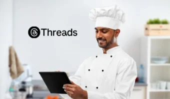 Un chef con uniforme y gorro blancos utiliza una tableta en una cocina. En la pared se puede leer la palabra "Threads" con un logotipo.