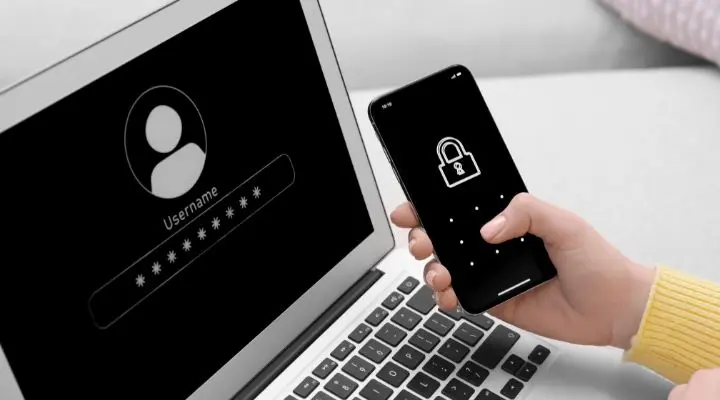 Una persona sostiene un teléfono inteligente con una pantalla bloqueada junto a una computadora portátil que muestra una pantalla de inicio de sesión con una contraseña oculta, lo que enfatiza la importancia de la privacidad de datos.