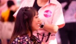 Mujer con cabello trenzado sonriendo, sentada junto a otra persona con una camisa rosa con el logo de una marca, en un entorno animado.