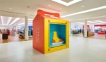 Gran expositor en forma de caja de zapatos con forma de zapatilla Converse, en medio de un centro comercial bien iluminado y rodeado de varias tiendas.