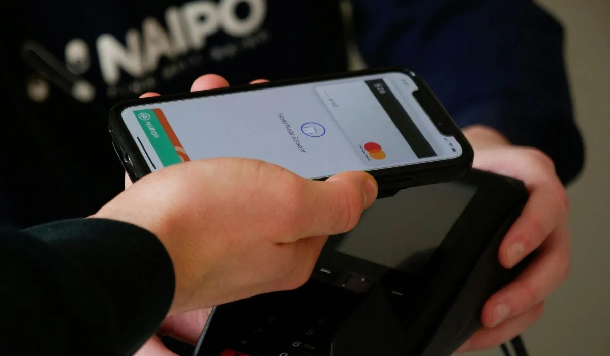 Una persona sostiene un teléfono inteligente cerca de una terminal de pago para realizar un pago sin contacto utilizando una aplicación de billetera digital, mostrando la conveniencia que ofrecen los neobancos en México.