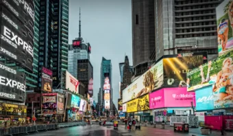 Times Square, en Nueva York, resplandeciente de brillantes vallas electrónicas y anuncios, exhibe un poderoso posicionamiento de marca mientras unas cuantas personas caminan por la calle húmeda y vacía.