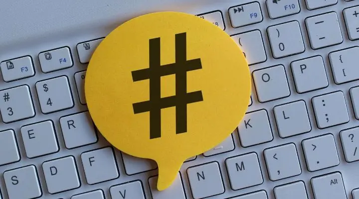 Una burbuja de diálogo amarilla con un símbolo de los hashtags negro reposa sobre un teclado de computadora blanco, lo que representa el poder de los hashtags efectivos para impulsar la participación en línea.