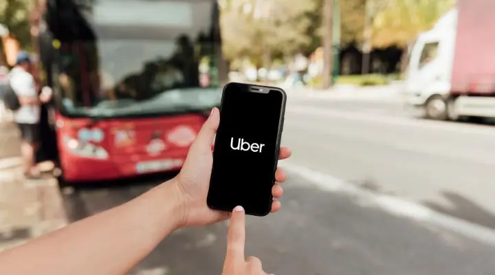 Una persona sostiene un teléfono inteligente con la aplicación Uber México abierta frente a un autobús rojo en una calle de la ciudad.