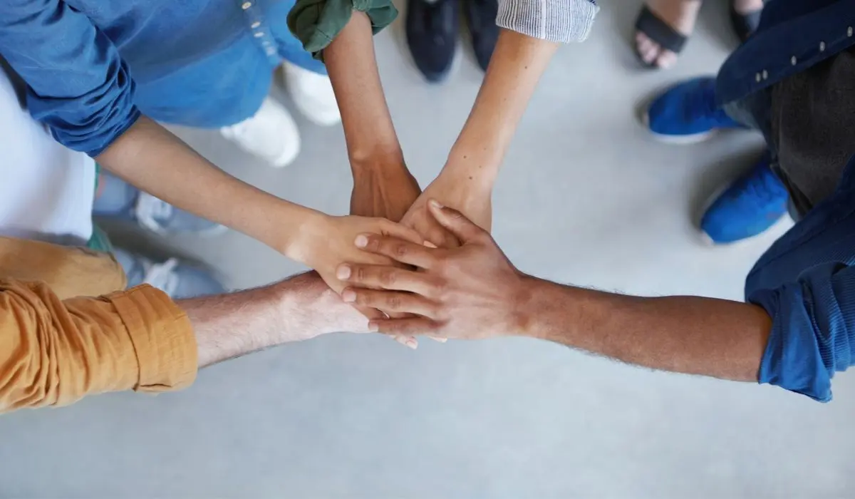 Un grupo de personas de pie en círculo con sus manos apiladas juntas en el centro, visto desde arriba, simboliza el poder del marketing colaborativo y el trabajo en equipo.