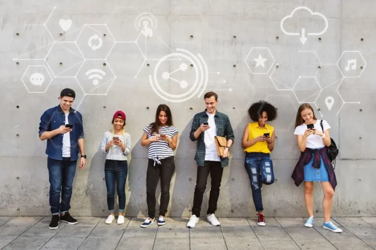 Seis personas están paradas frente a una pared, cada una mirando su teléfono inteligente, con íconos de redes digitales ilustrados sobre ellos: un verdadero sello millennial.