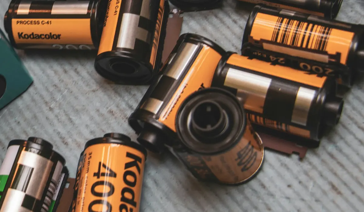 Varios rollos de película Kodak de 35 mm están dispersos en una superficie de textura ligera, con botes de película y etiquetas visibles: un guiño perfecto al regreso de Kodak a la fotografía analógica.