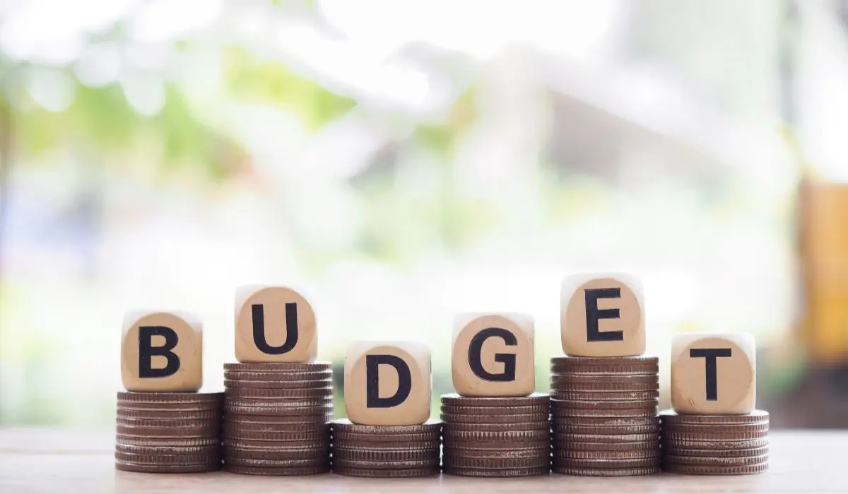 Se colocan bloques de madera que forman la palabra "BUDGET" sobre pilas de monedas, resaltando el concepto de presupuesto limitado sobre un fondo natural borroso.