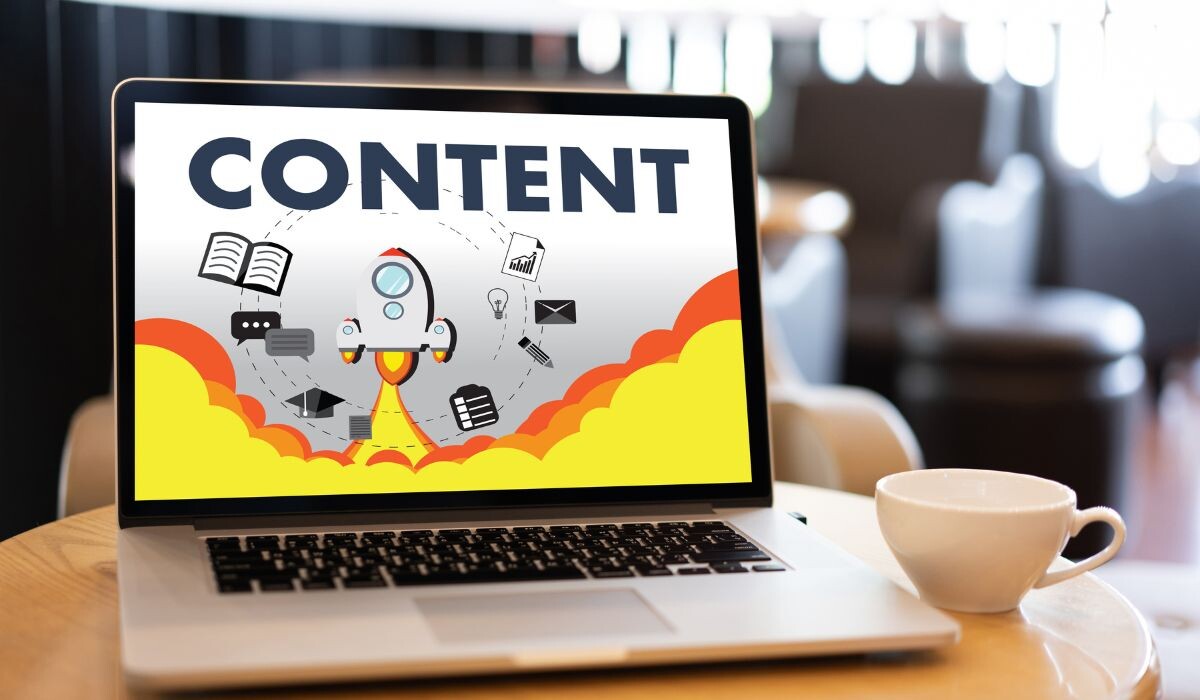 Una computadora portátil sobre un escritorio que muestra un gráfico colorido con la palabra "contenido evergreen" y varios íconos multimedia, junto a una taza de café.