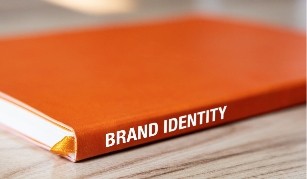 Un libro naranja titulado “IDENTIDAD DE MARCA” yace sobre una superficie de madera.