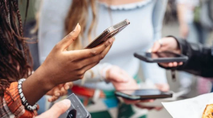 Varias personas se encuentran juntas, cada una sosteniendo y mirando sus teléfonos inteligentes, como si estuvieran pensando en una estrategia de marketing online.