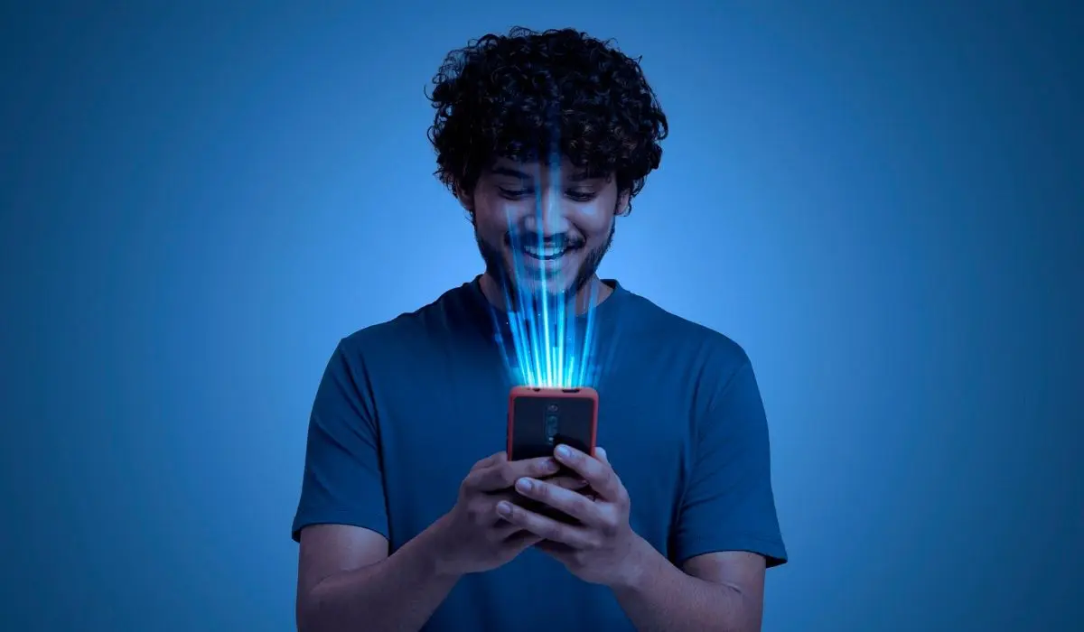 Una persona mira un teléfono inteligente en un entorno oscuro, con rayos de luz azules iluminando su rostro.