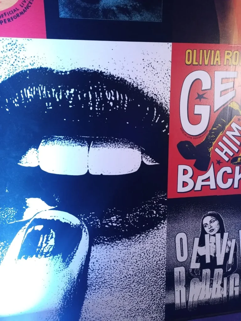 Primer plano de una imagen pop art en blanco y negro de unos labios y un dedo. Junto a ella, un texto vibrante y colorido exclama: "¡ Olivia Rodrigo: Recuperadlo!".