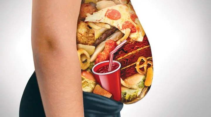 El perfil lateral de una persona muestra una sección transparente que revela una variedad de comida chatarra, con pizza, hamburguesas y refrescos en su interior.