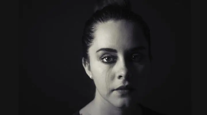 Una mujer con el cabello recogido mira directamente a la cámara con poca luz, con visibles lágrimas en su rostro sobre un fondo oscuro: una imagen impactante que captura el poder puro del marketing emocional.