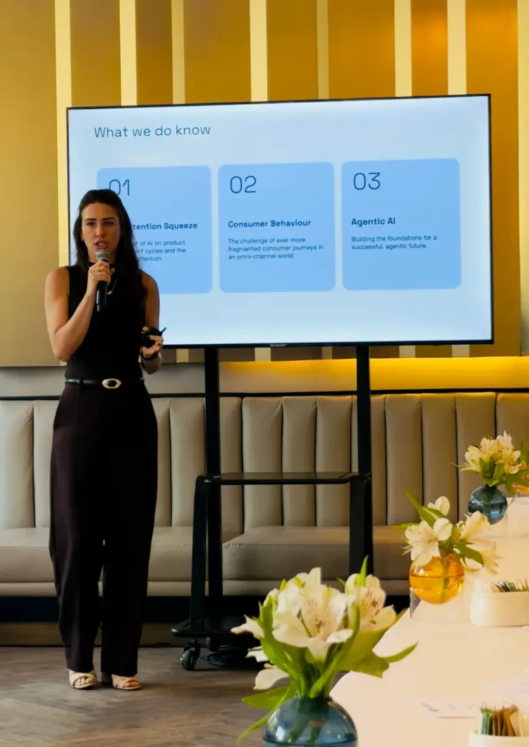 Renata Altemari de AppsFlyer, con un micrófono en la mano, presenta delante de una pantalla que muestra tres secciones -Retention Squeeze, Consumer Behaviour y Agentic AI- en una moderna sala de conferencias, mostrando el mercado móvil mexicano